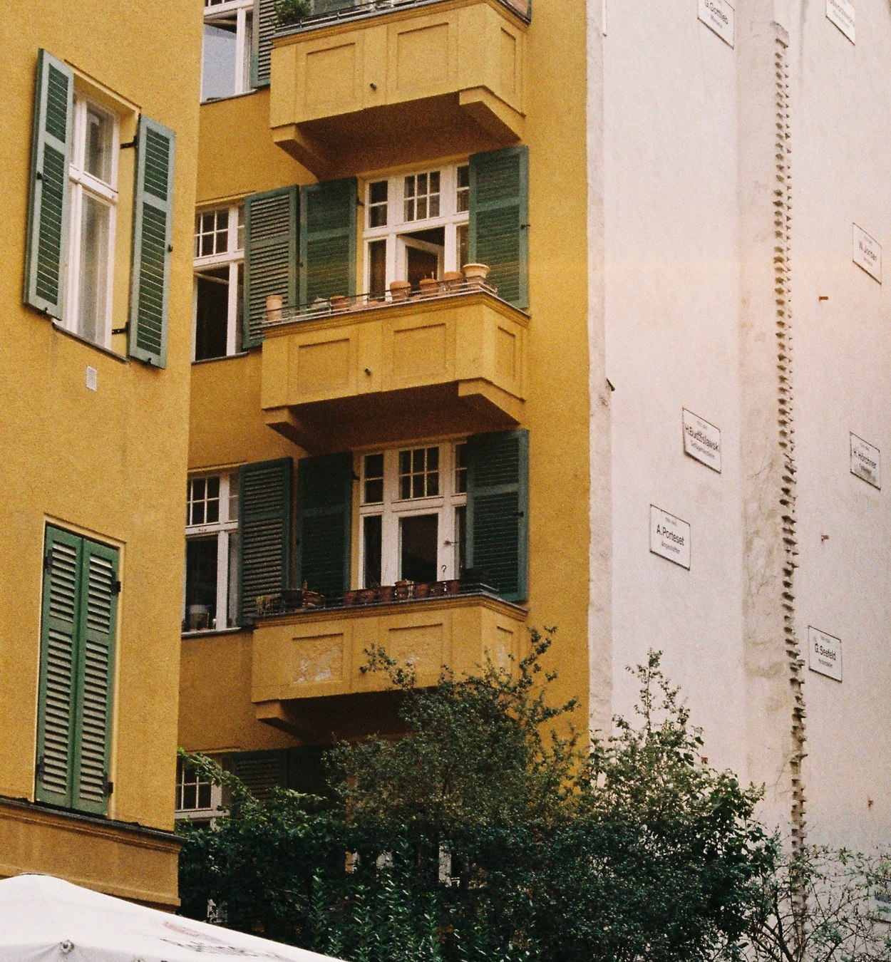 Gelbe Berliner Wohnhausfassade mit Balkonen und grünen Fensterläden