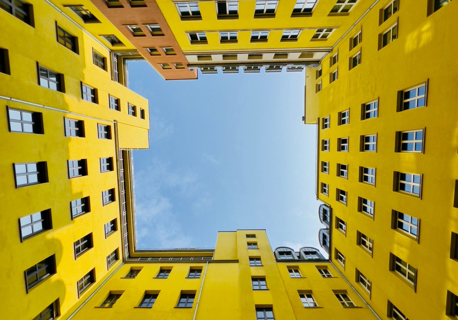Gelber Berliner Innenhof mit vielen Fenstern und blauem Himmel